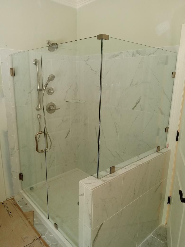Corner glass shower enclosure with marble-look tile, silver fixtures, and a low curb.