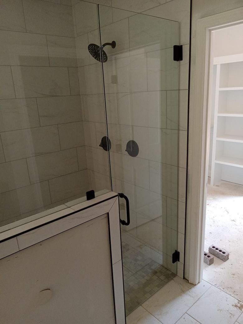 Glass shower enclosure with black hardware, white tiled walls, and a doorway to a room with shelves.