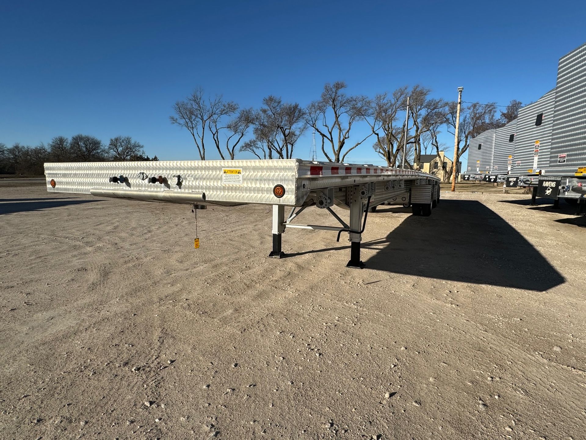 A flatbed trailer is parked in a dirt lot with trees in the background.