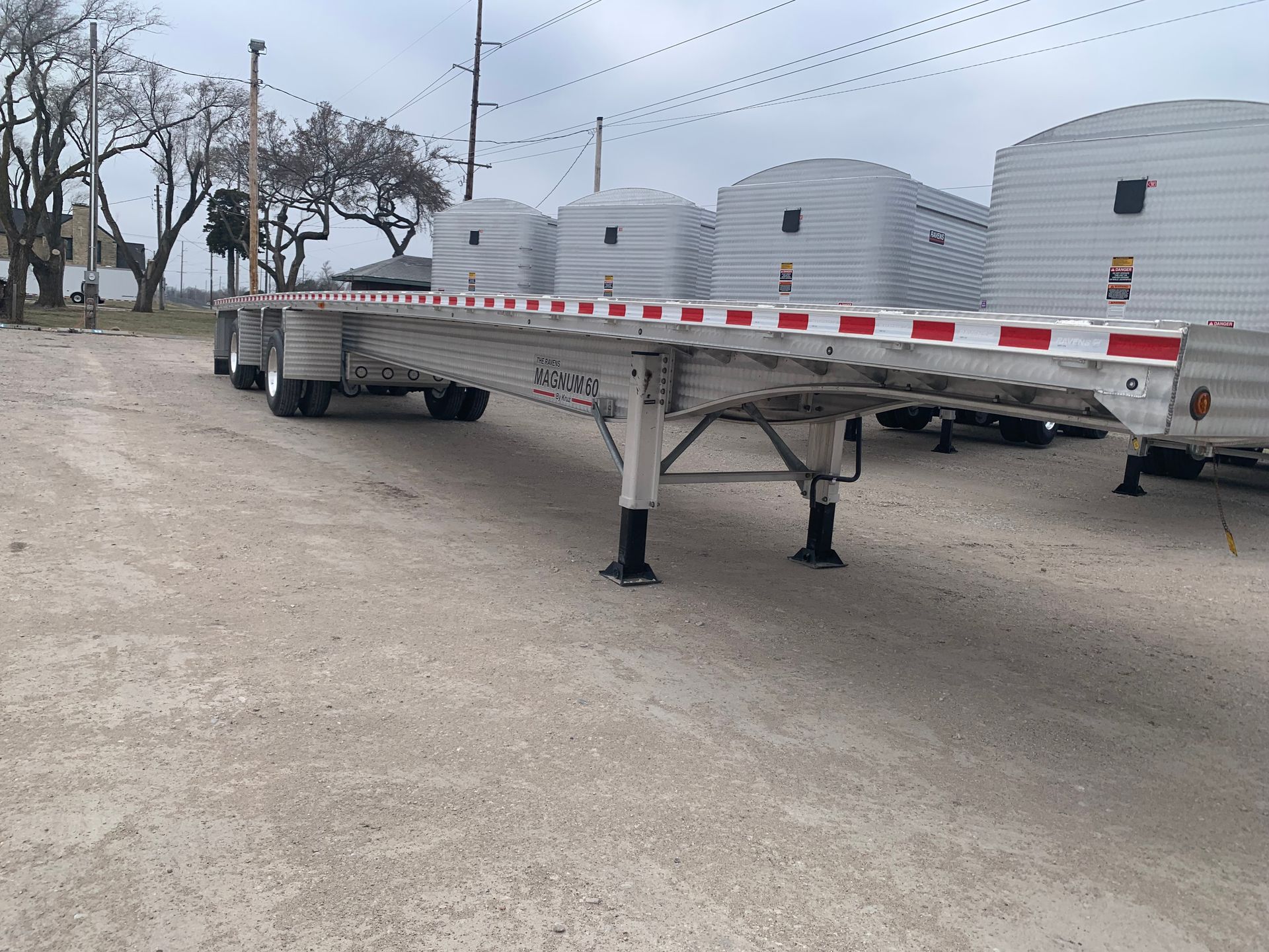 A trailer with a red and white stripe on the side is parked in a gravel lot.