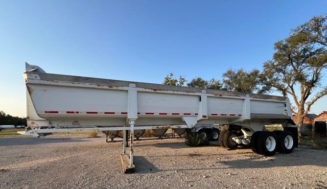 A white semi truck with a black fender is parked in a parking lot
