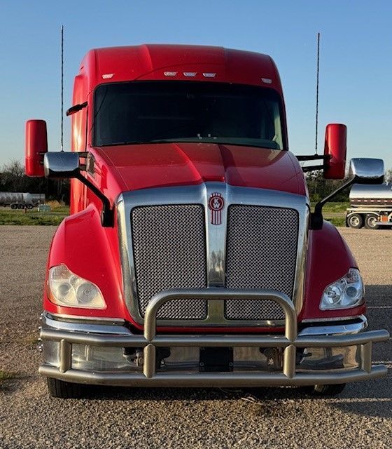 A red kenworth semi truck is parked in a gravel lot
