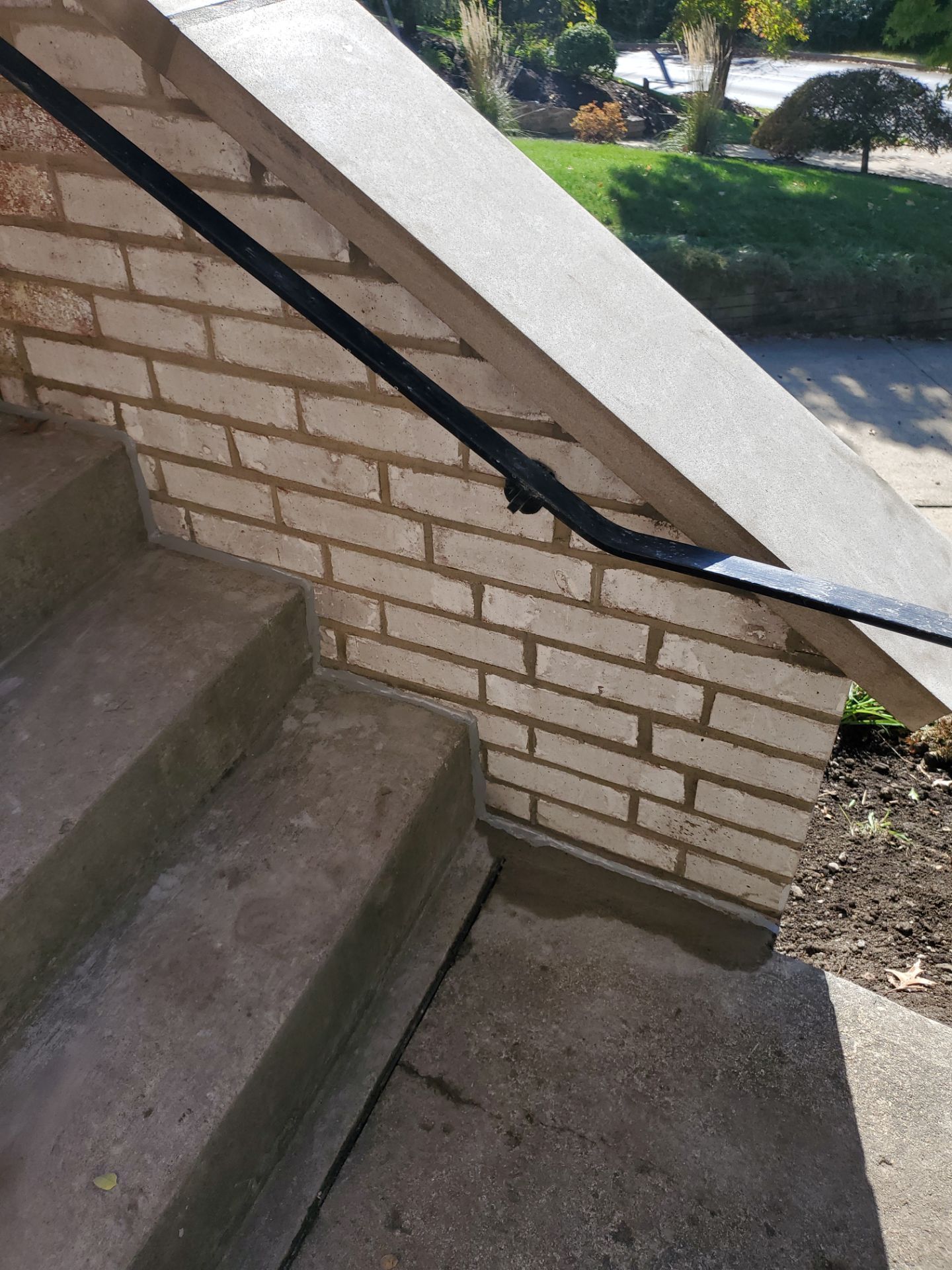 Concrete steps with brick side and black handrail, leading up to a landing.