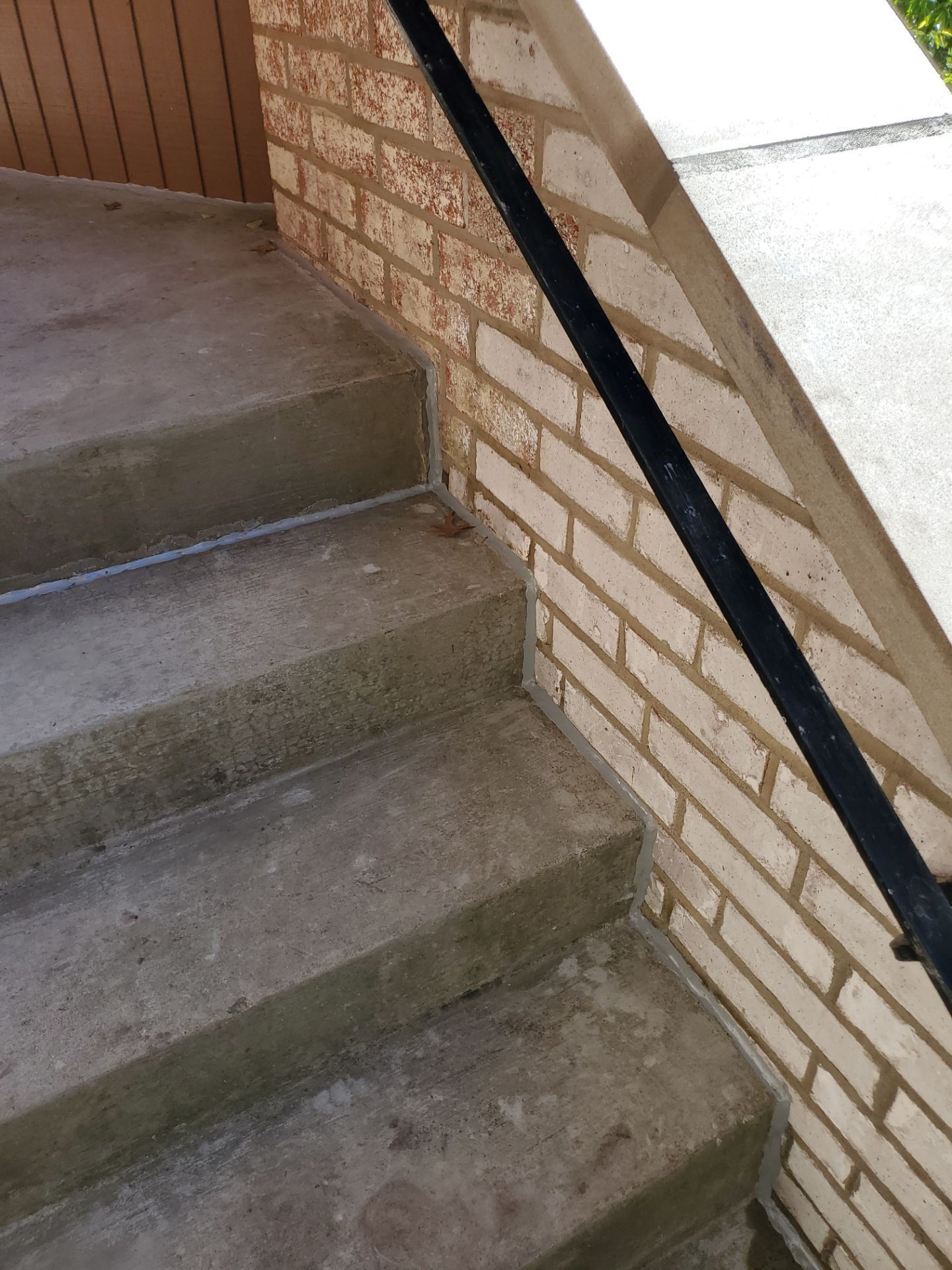 Concrete steps with a black handrail and brick wall.