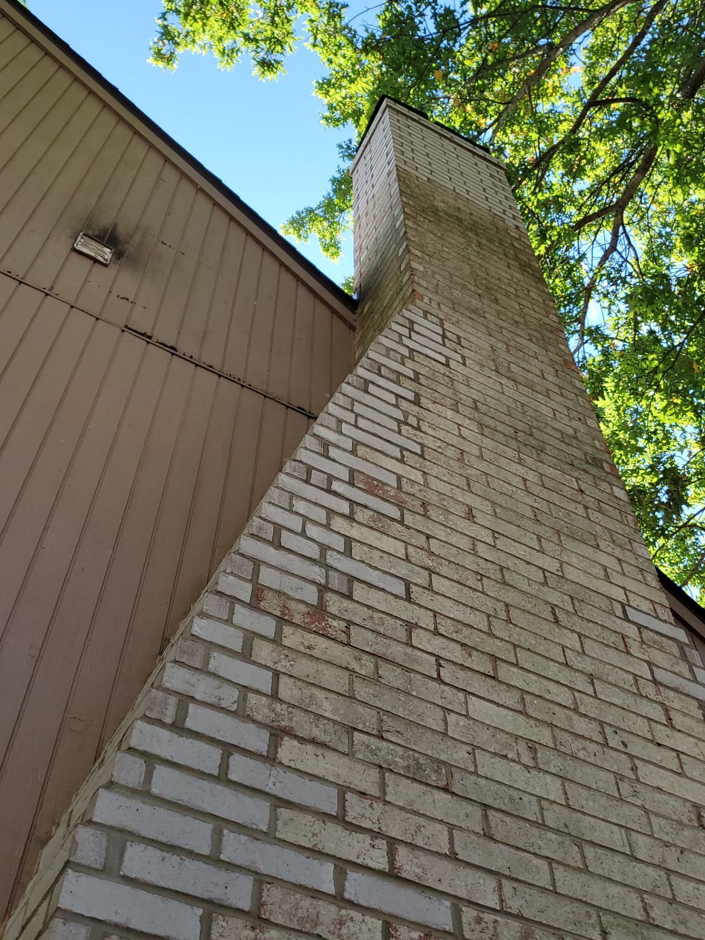 Brick chimney against a brown building; green trees in the background, blue sky visible.
