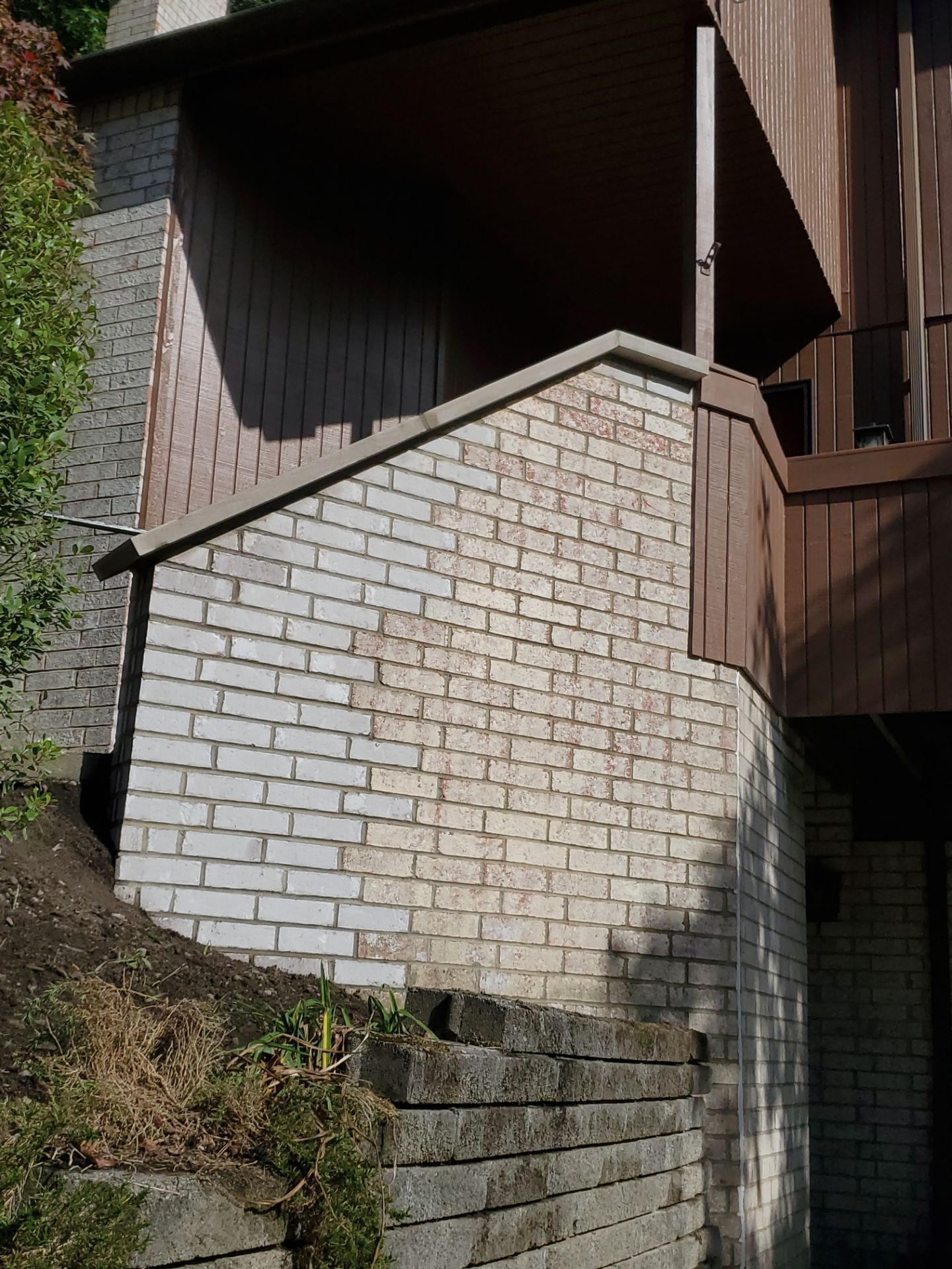 Brick retaining wall and stairs leading up to a wooden deck, next to a building's exterior.