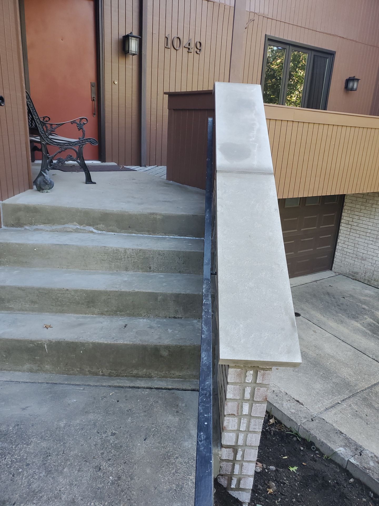 Concrete steps leading up to a brown door with a metal railing on the side.
