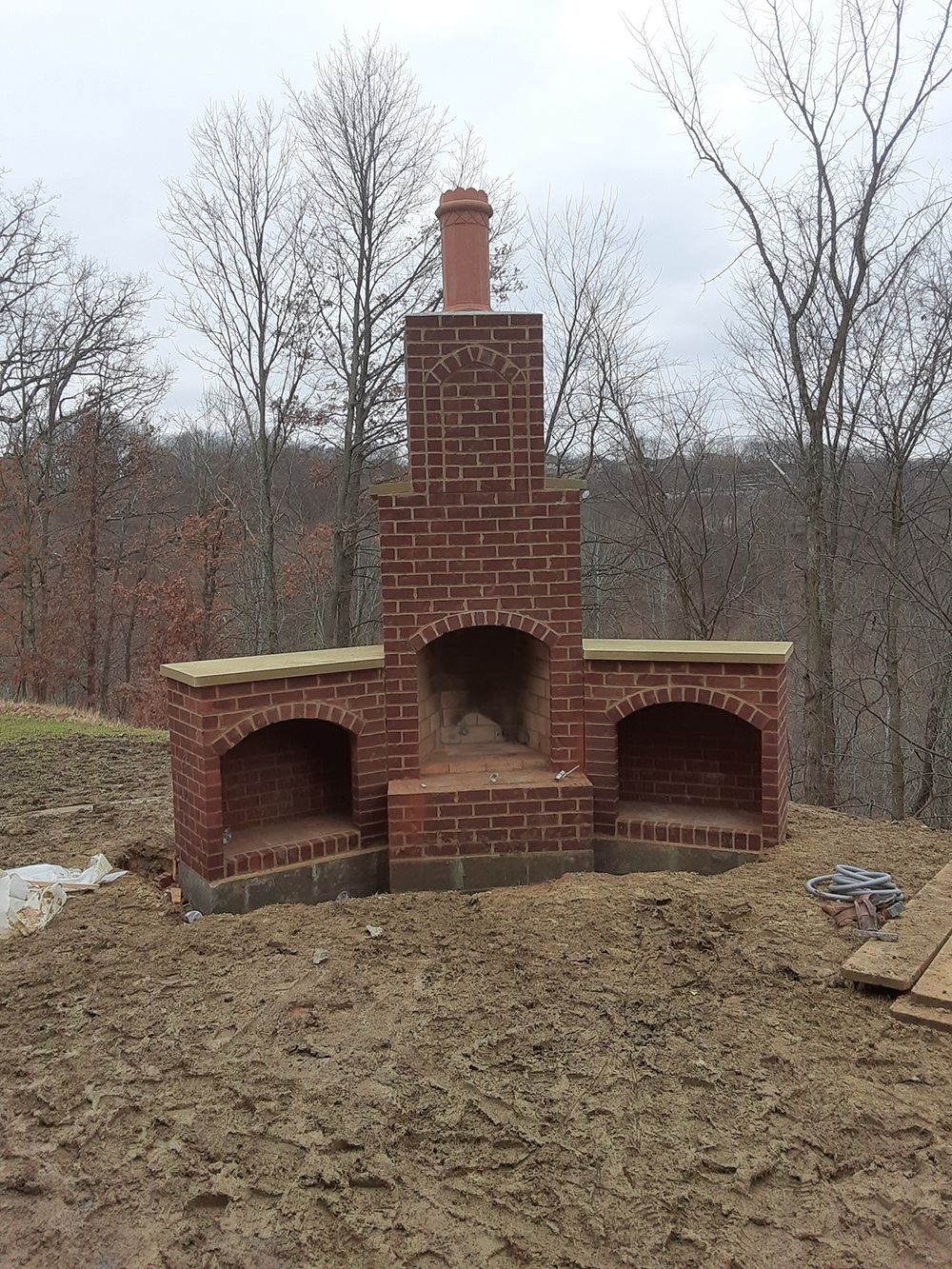 Red brick outdoor fireplace with two side alcoves and a tall chimney.