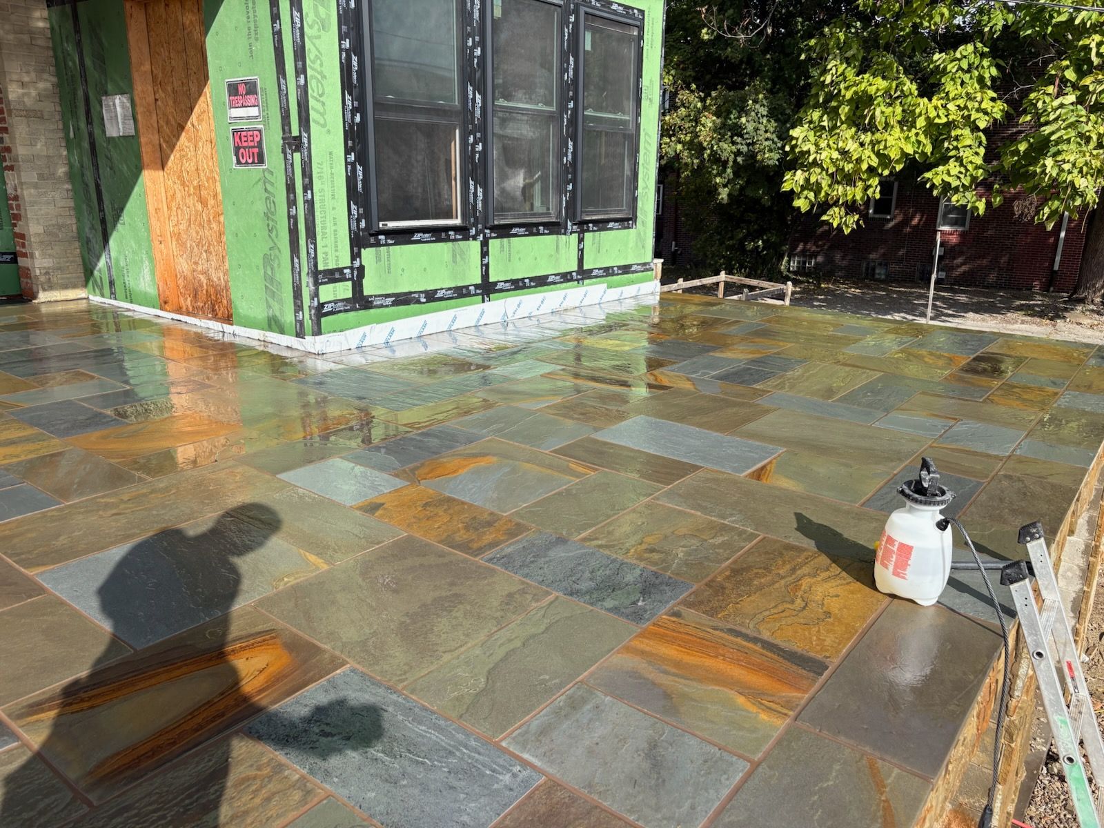 Newly installed stone patio with wet, colorful tiles. Building with black windows in background.