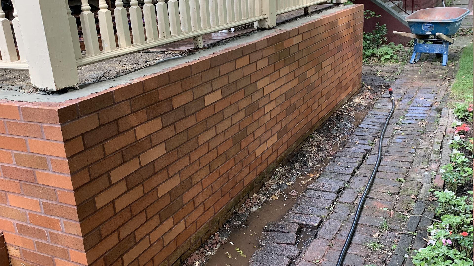 Brick wall under a white railing with a brick path beside it; wet with debris.