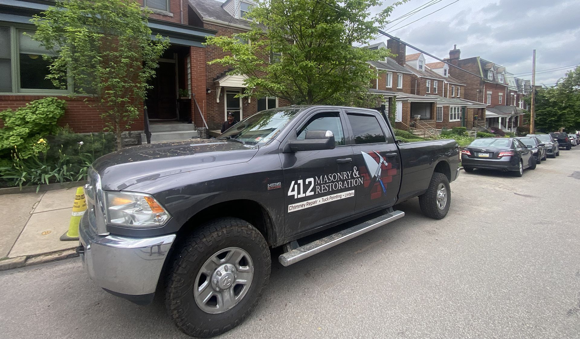 Dark gray pickup truck parked on a street in front of brick buildings; the truck has company logo.