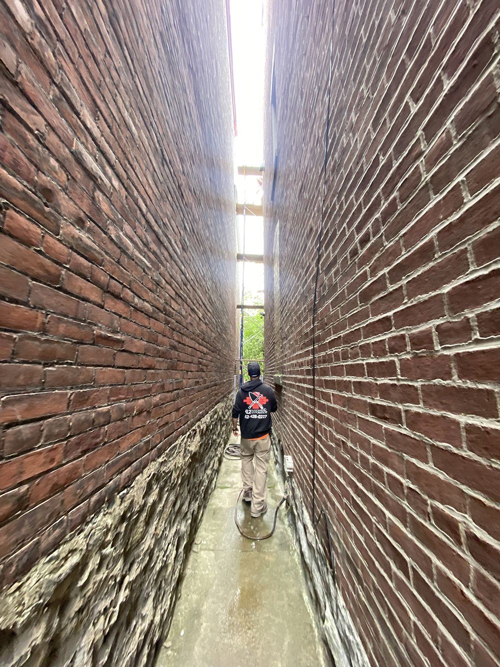A person walks in a very narrow alley between two red brick walls.
