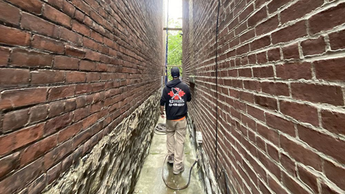 Person power washing a narrow brick alley.