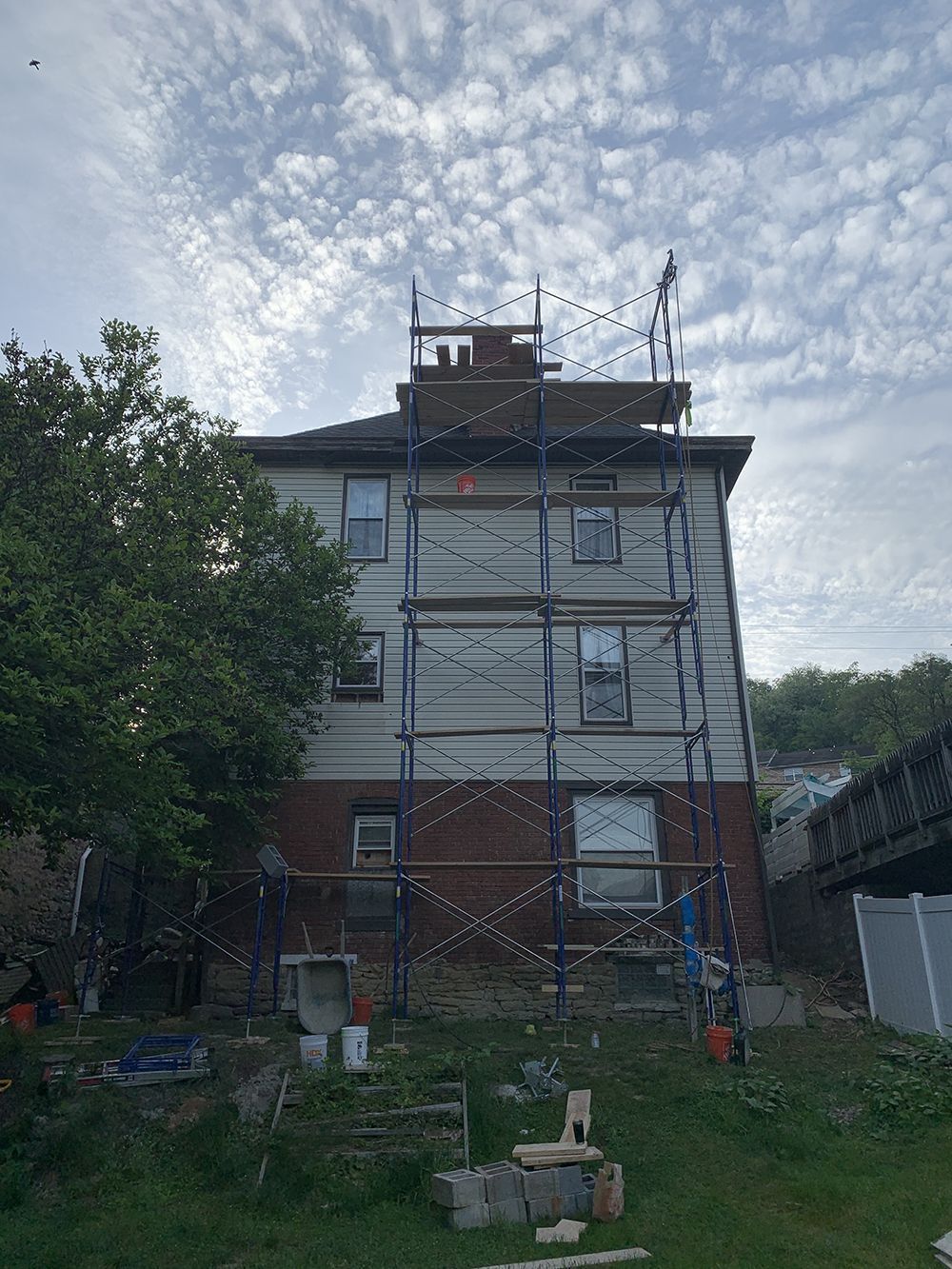 Building under construction, scaffolding wraps the three-story structure. A brick base, light siding and chimney.