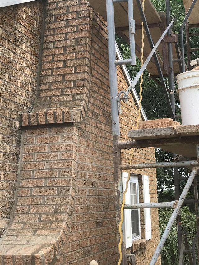 Brick chimney under repair, scaffolding, white bucket, and window.