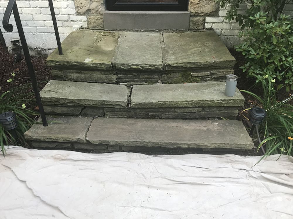 Stone steps leading to a doorway. Steps are cracked and uneven. Handrail is present.