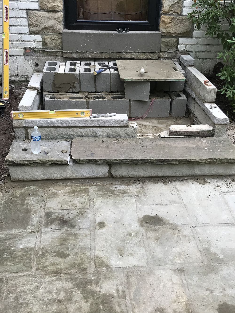Construction of outdoor concrete steps, with blocks and slabs in progress. A water bottle and level are visible.