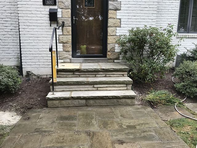 Stone steps leading to a front door of a house with light brick siding and a small bush.
