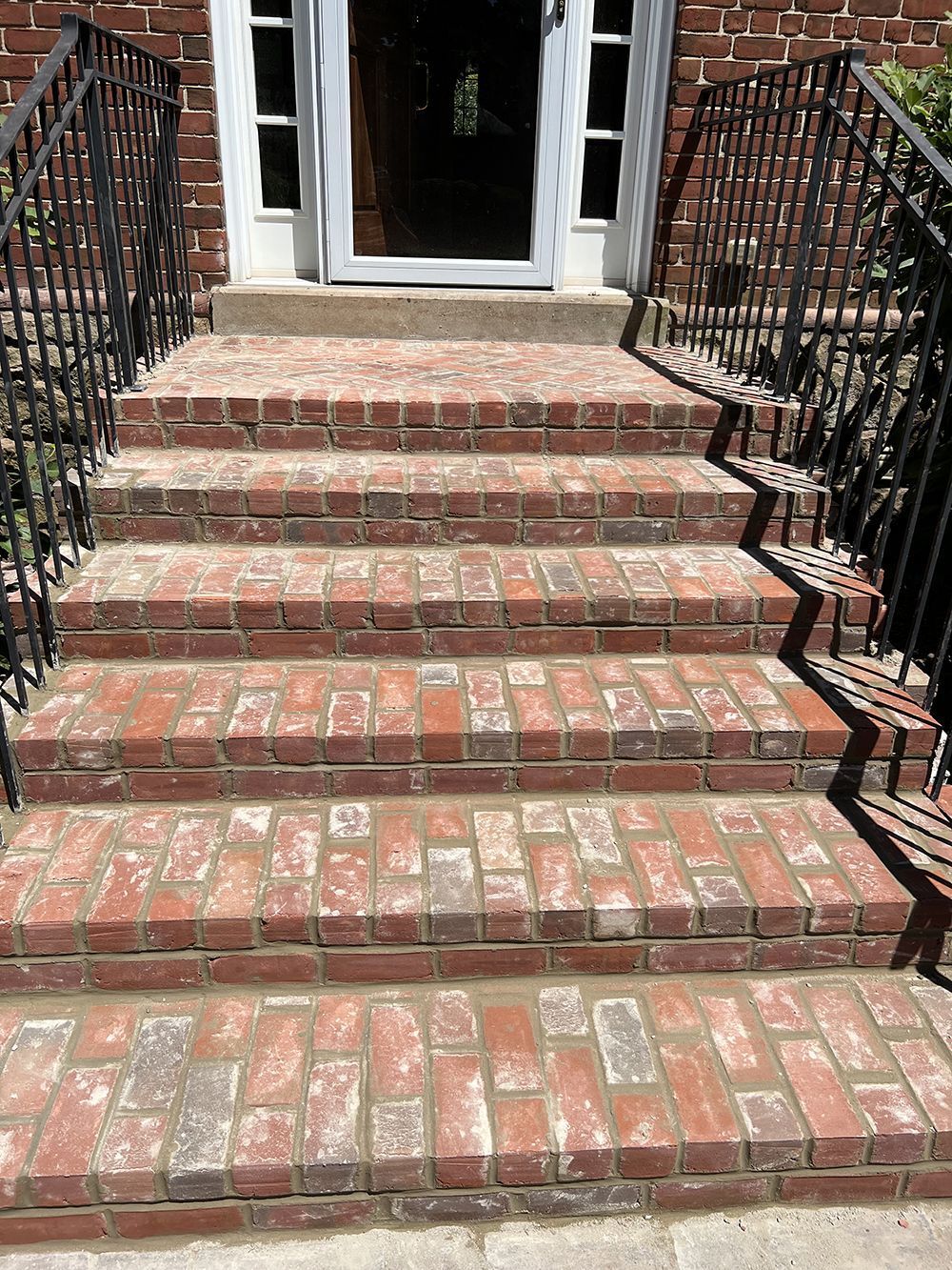 Brick steps leading to a white door with black railing on either side.