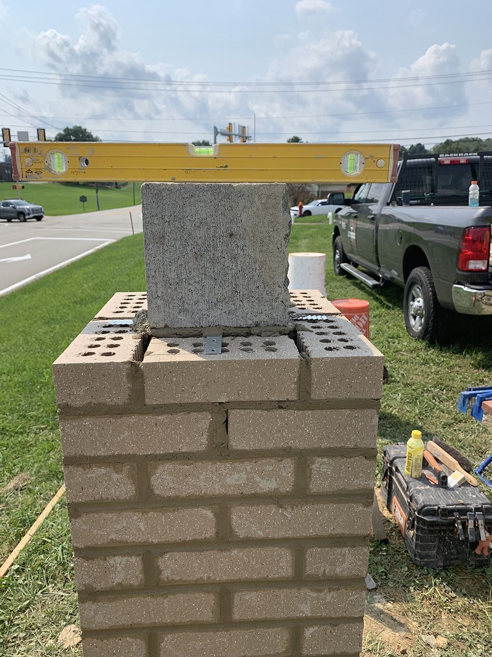 Masonry work in progress; bricks being laid. A level rests on top, and a truck is in the background.