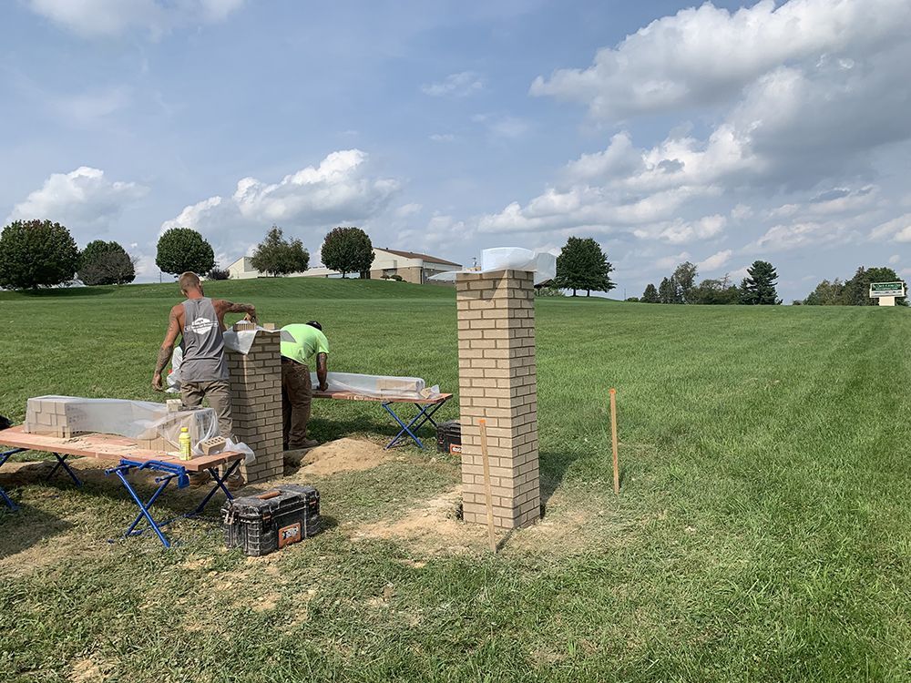 Bricklayers constructing a brick structure in a grassy field on a sunny day.