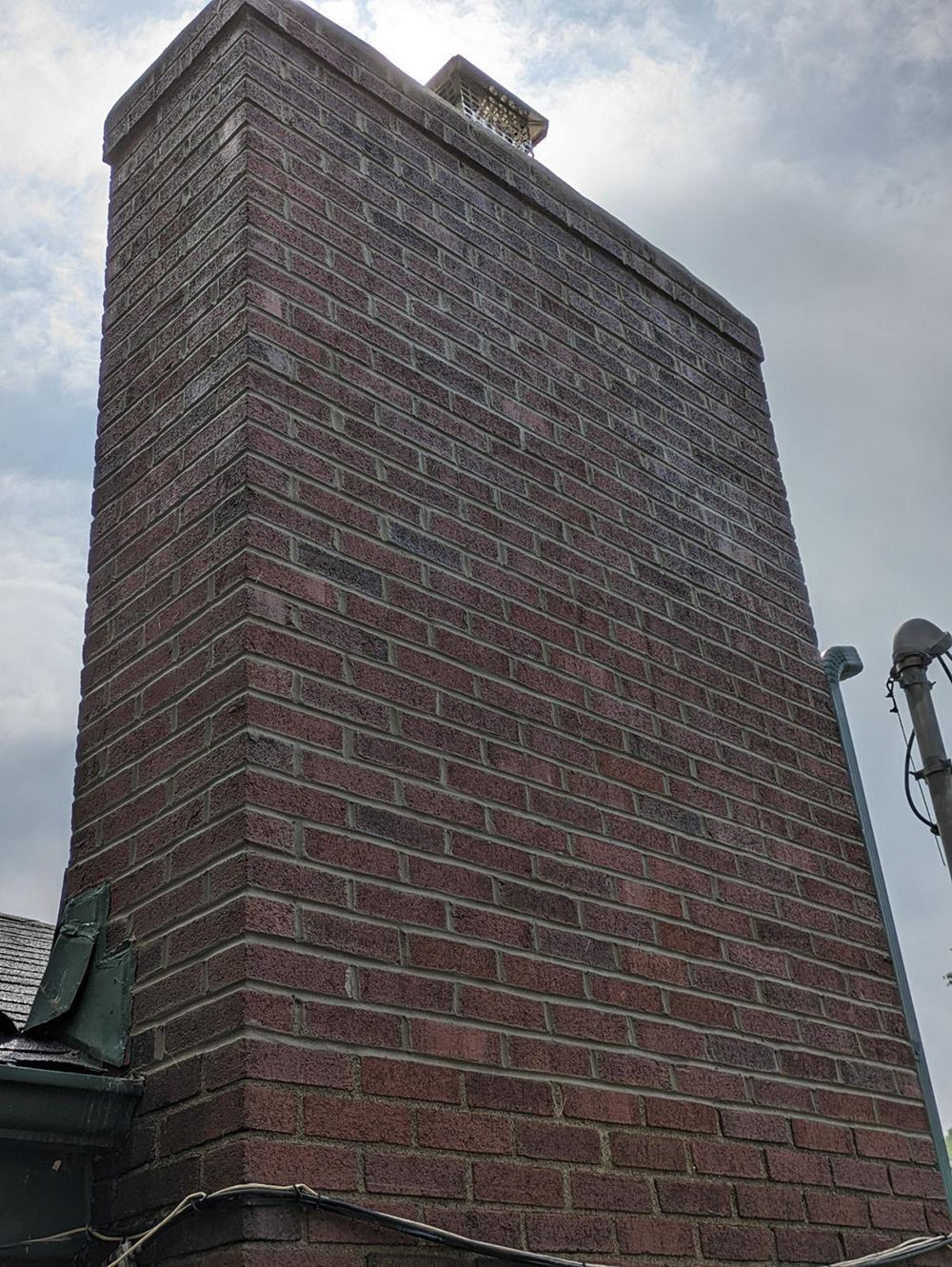 Tall red brick chimney against a cloudy sky.