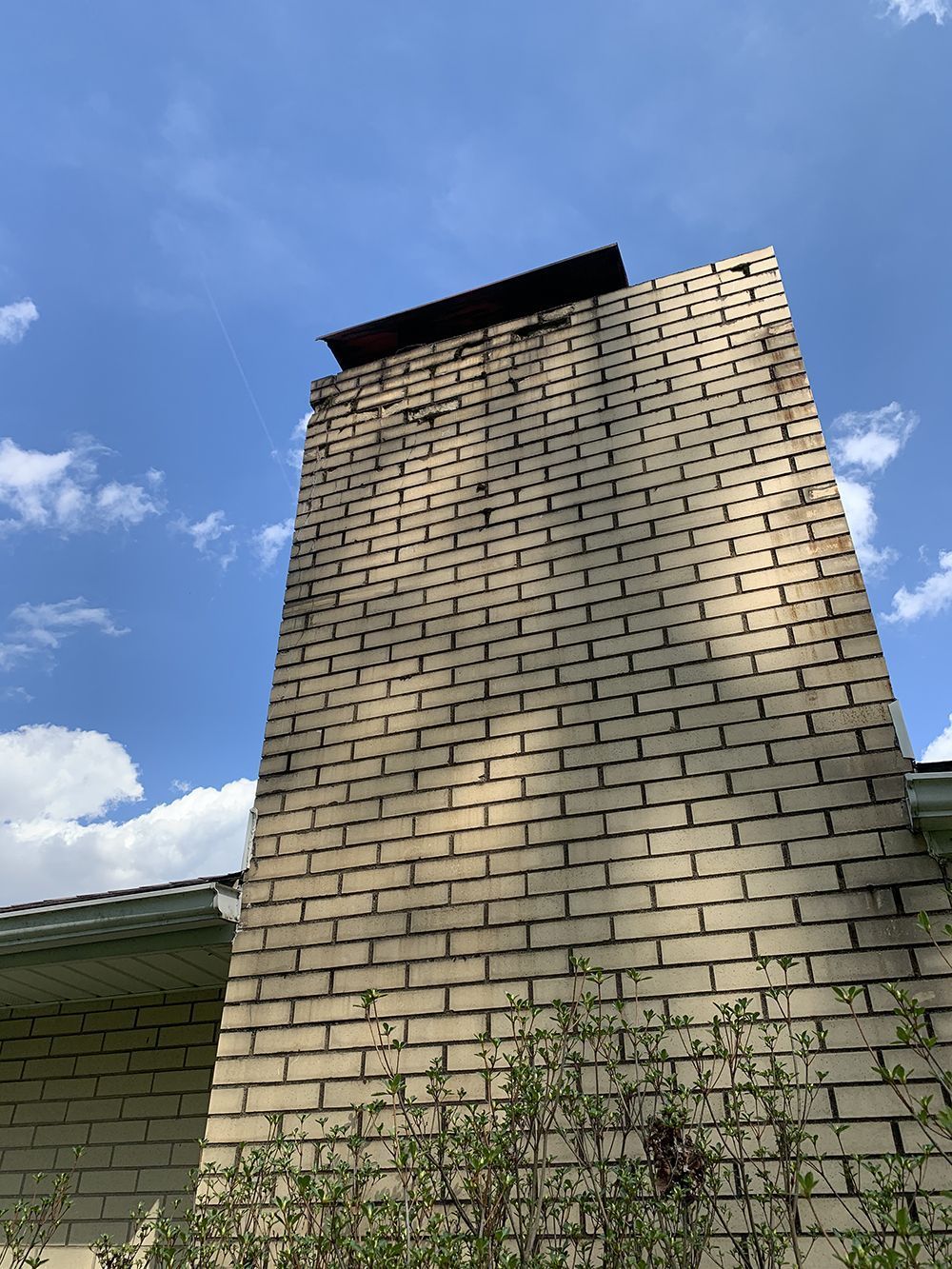 Tall brick chimney against a blue sky, topped with a dark, rectangular cap.