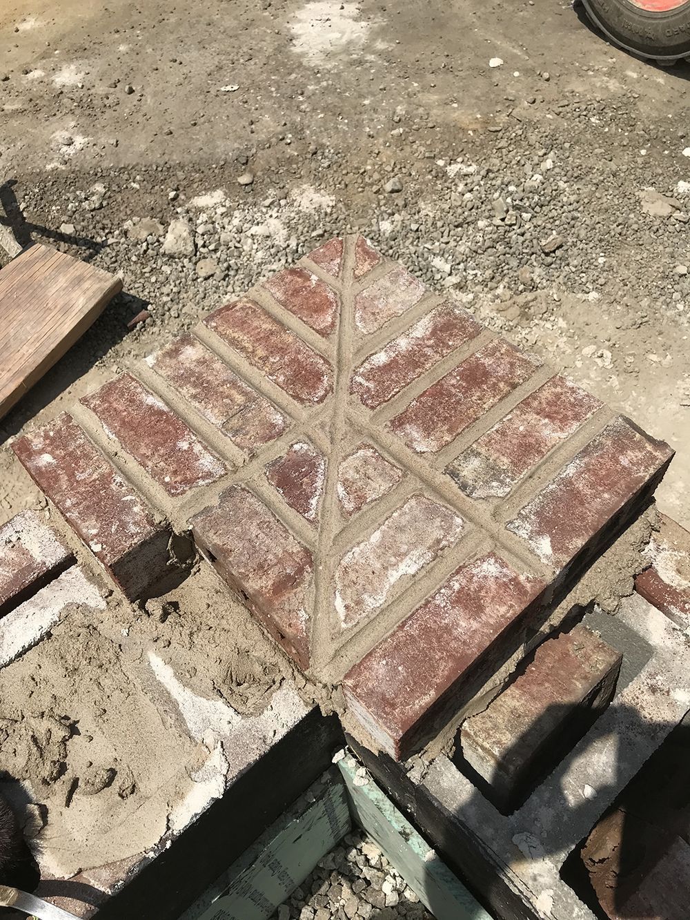 Brick pathway under construction; red bricks in a patterned design, surrounded by mortar.