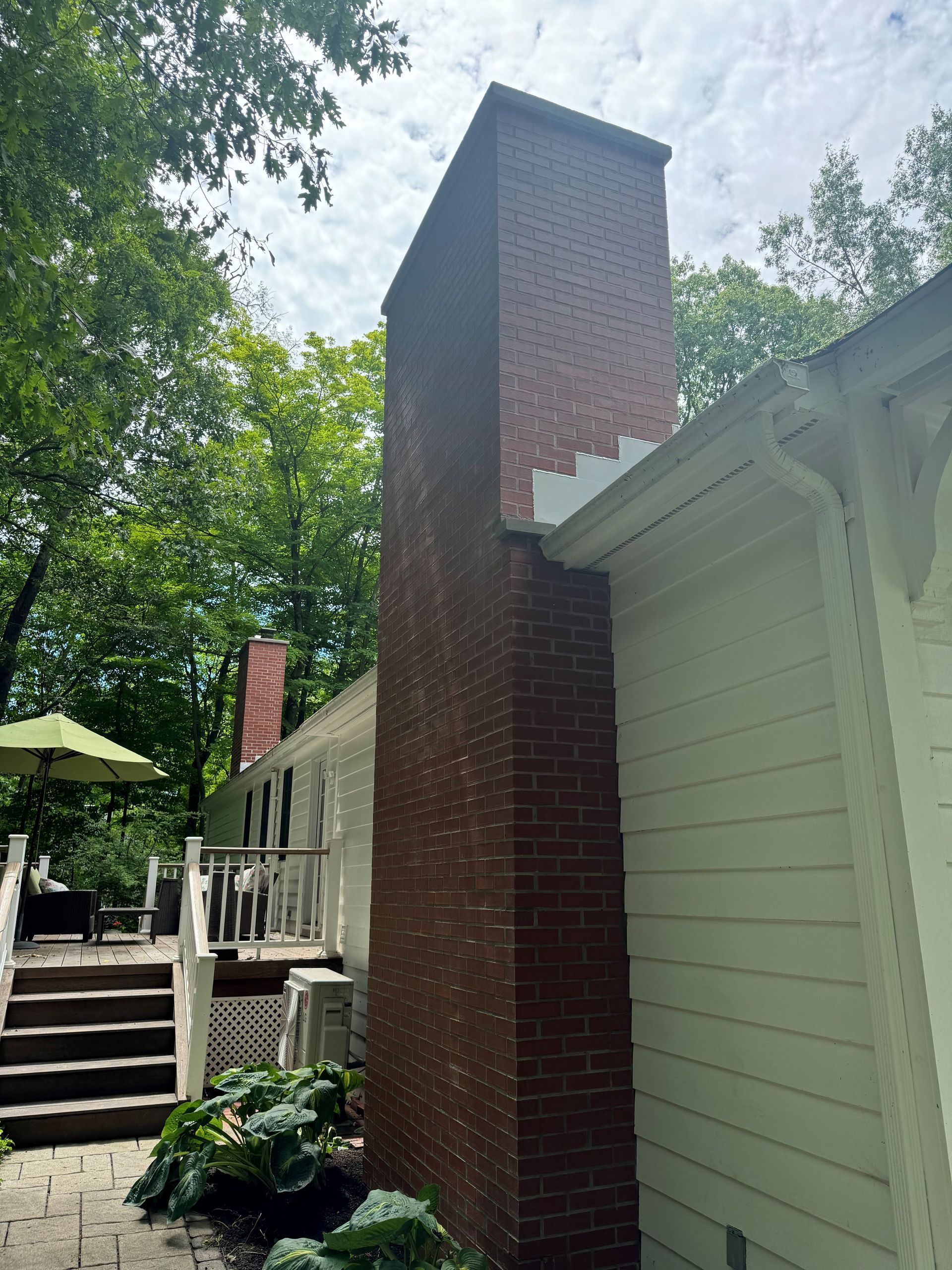 Brick chimney against white siding and green foliage.