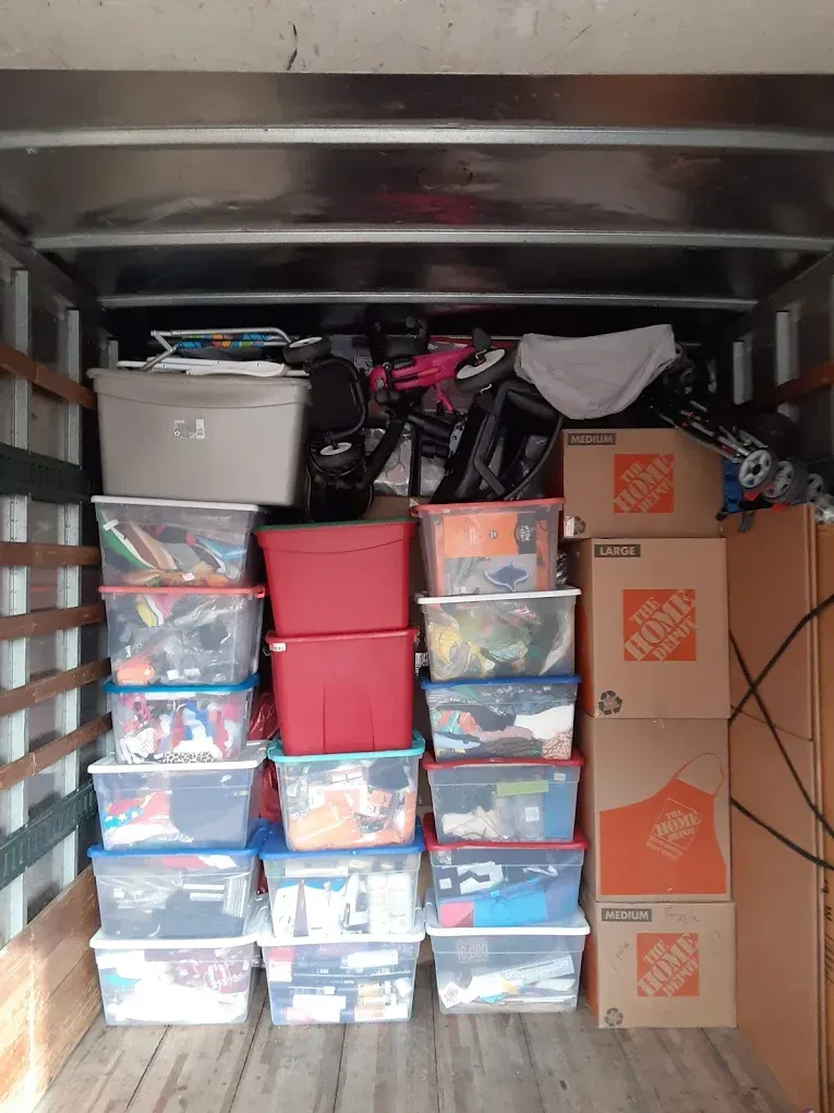 Inside of a moving truck, stacked plastic bins, cardboard boxes, and various items.