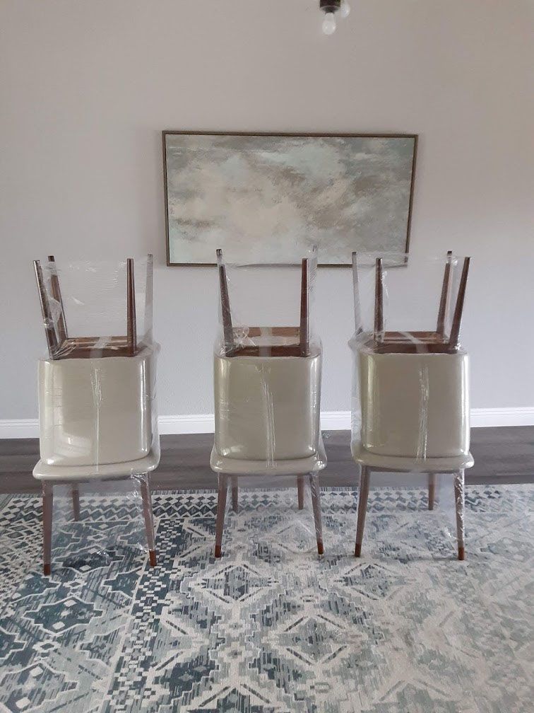 Three chairs, legs up, stand on patterned rug beneath artwork, against gray wall.