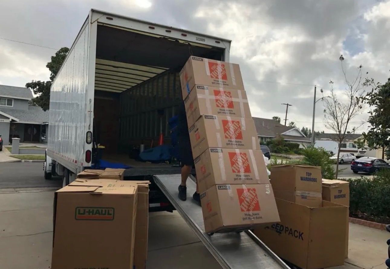 Moving boxes being loaded onto a truck via a ramp in a driveway.