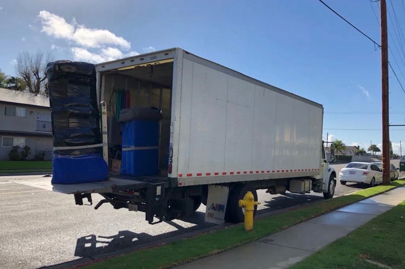 A moving truck with its back door open, parked on a street near a sidewalk.