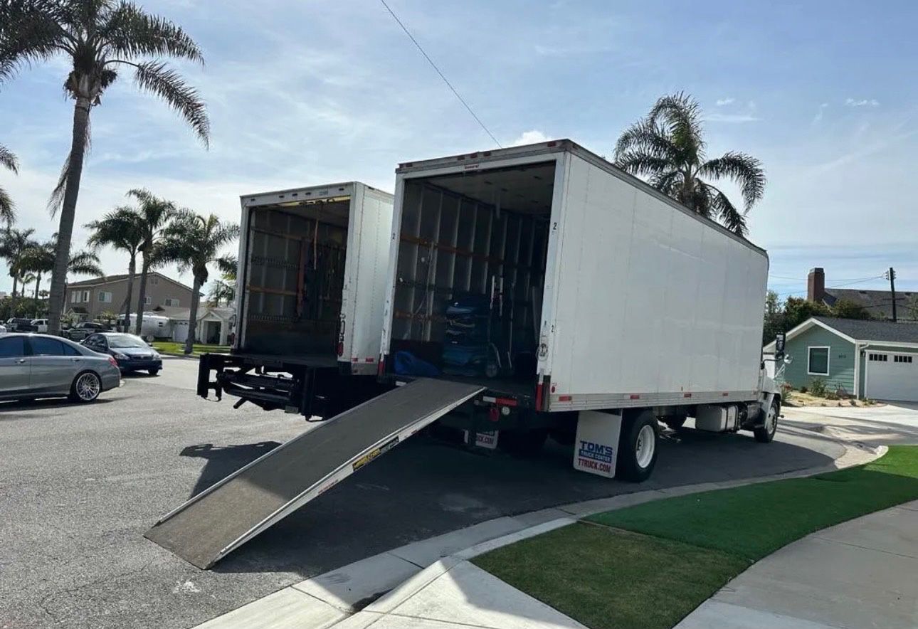 Two white moving trucks with ramps open on a residential street.