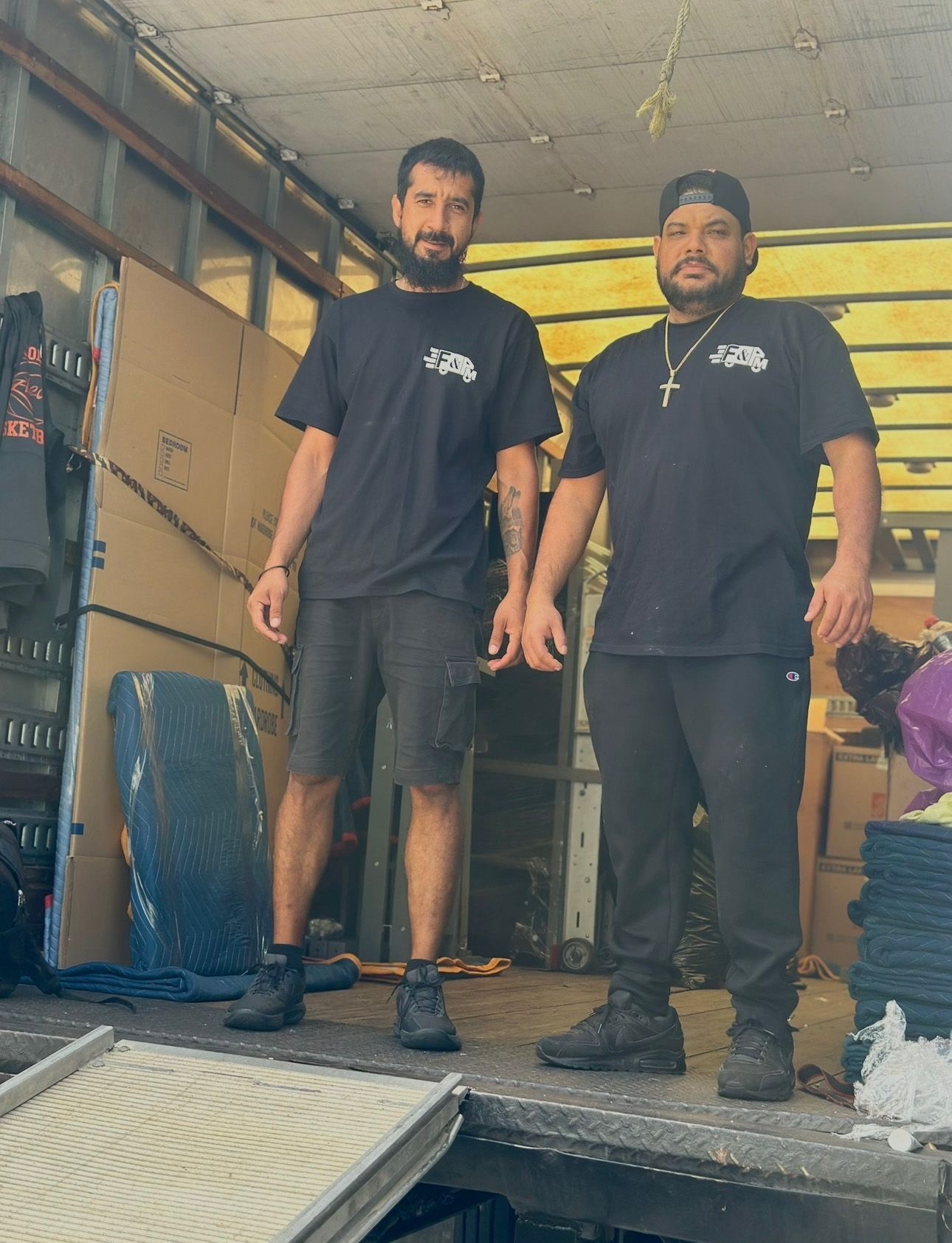 Two men in black shirts inside a moving truck, holding hands. They appear to be movers, preparing to unload.
