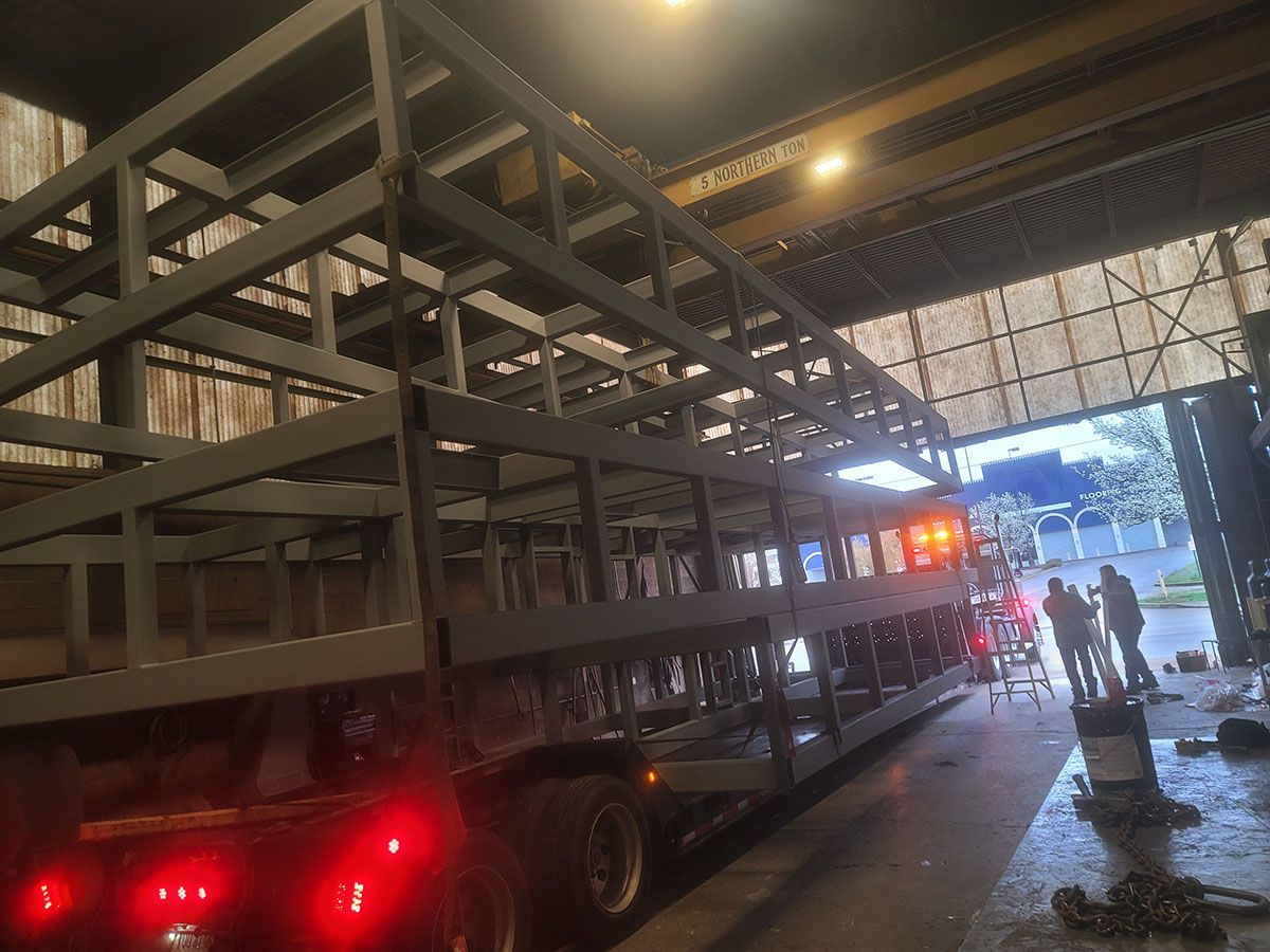 A truck is carrying a large metal structure in a warehouse.