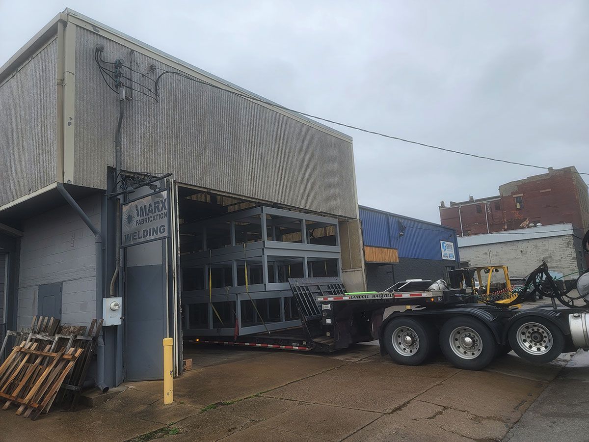 A semi truck is parked in front of a building with its doors open.