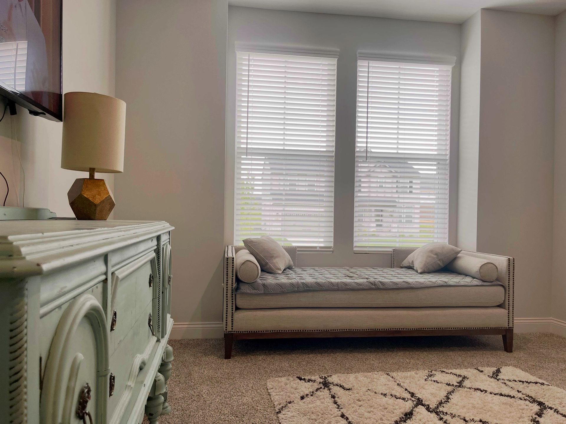 A living room with a day bed, dresser, lamp, and television.