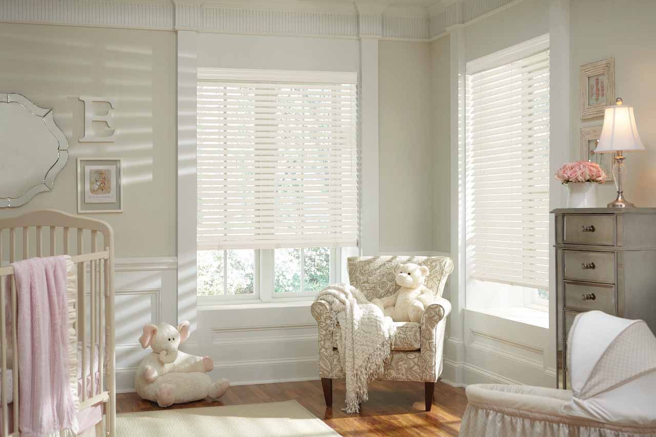 A baby room with a crib , chair , and window with blinds.