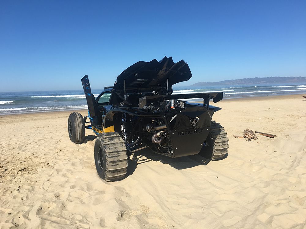 A blue atv is driving through the sand on a dirt road.