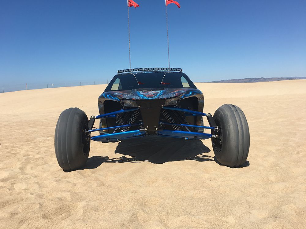 A blue atv is driving through the sand on a dirt road.