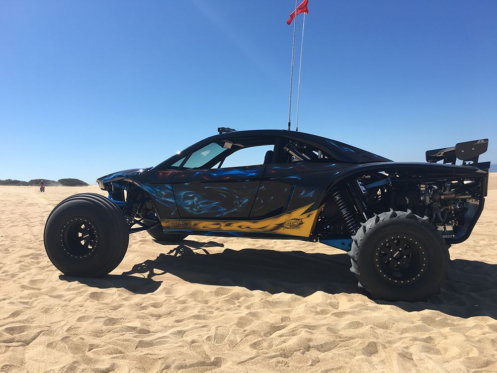 A blue atv is driving through the sand on a dirt road.