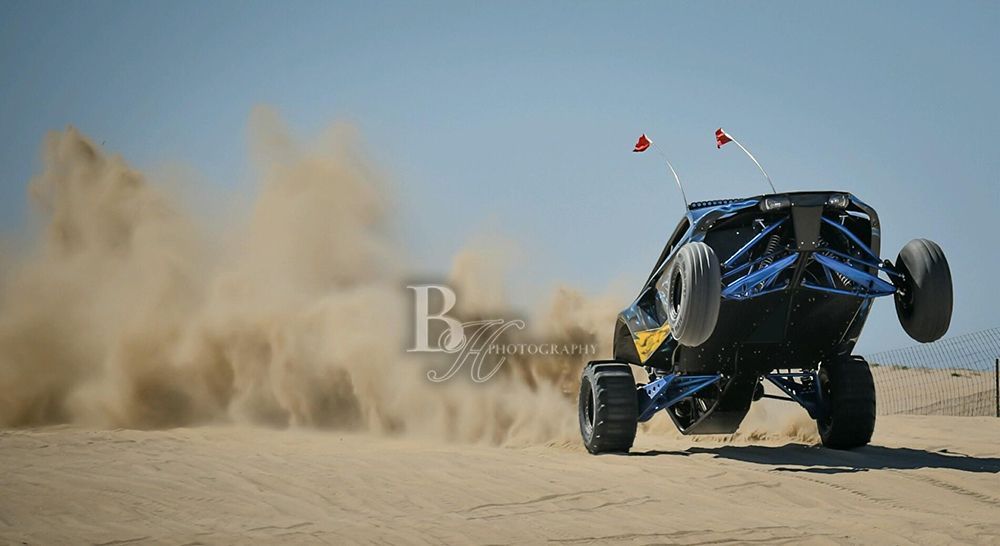 A blue atv is driving through the sand on a dirt road.