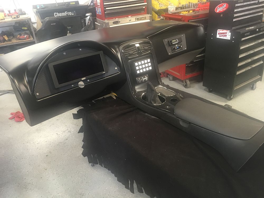 The dashboard of a car is sitting on the floor in a garage.