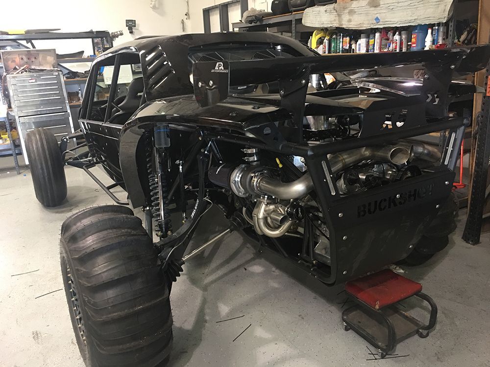A black dune buggy is sitting on a lift in a garage.