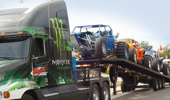 A monster truck is carrying a trailer full of buggies.