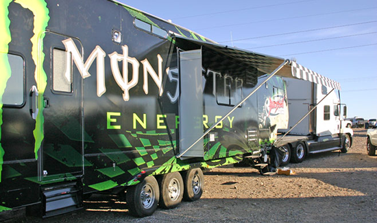 A monster energy trailer is parked in the dirt.