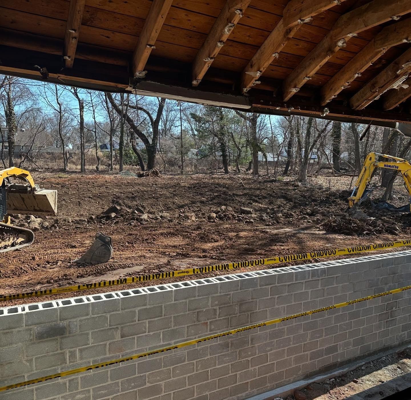 Construction site: Excavators moving dirt near a cinder block wall, viewed from inside a structure.