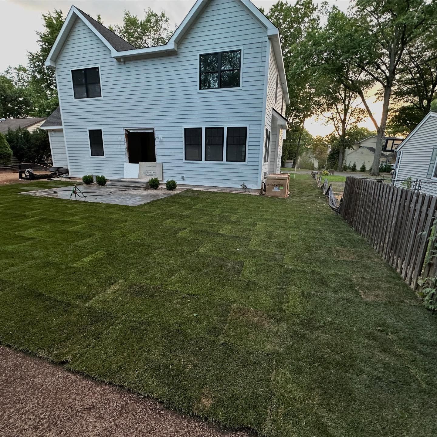 Newly sodded lawn in front of a light blue house, with a wooden fence on the right.