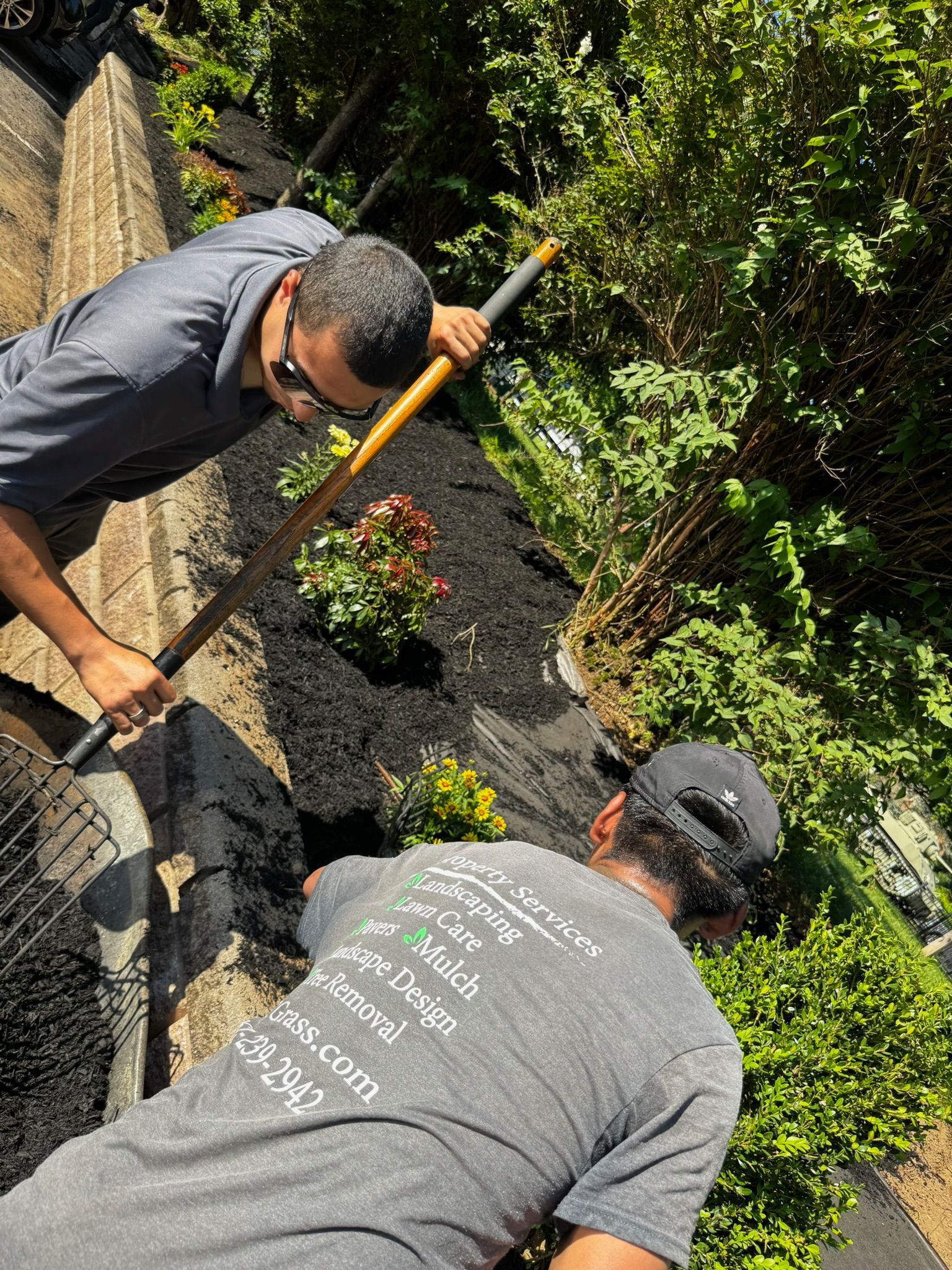 Two men mulching a garden bed with a shovel.